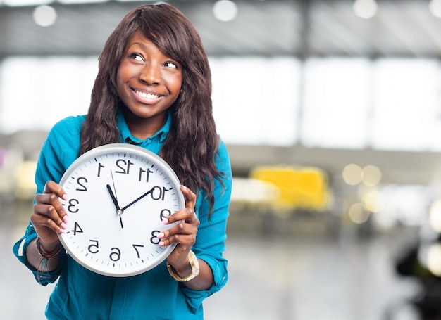 Chica alegre sujetando un reloj y mirando hacia arriba