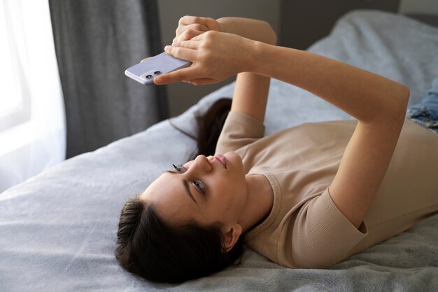 Chica de alto ángulo en la cama con teléfono inteligente