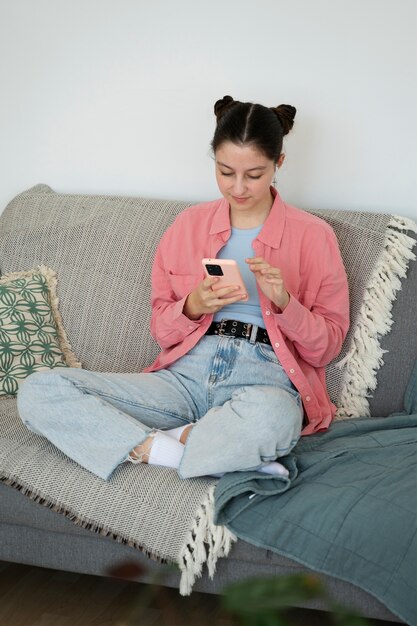 Chica de alto ángulo en el sofá con teléfono inteligente