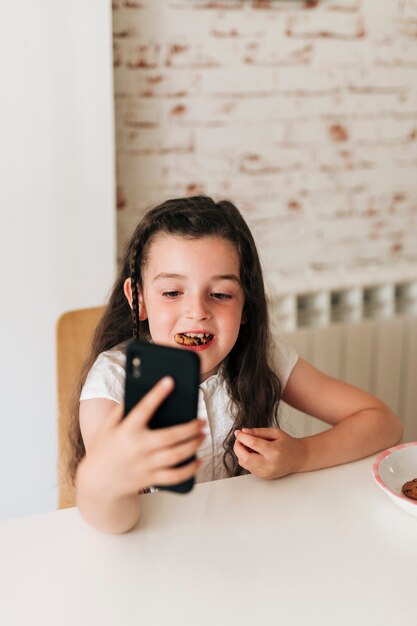 Chica de alto ángulo con teléfono comiendo galletas