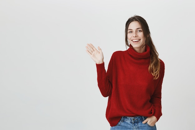 Chica amable en suéter agitando la mano, saluda