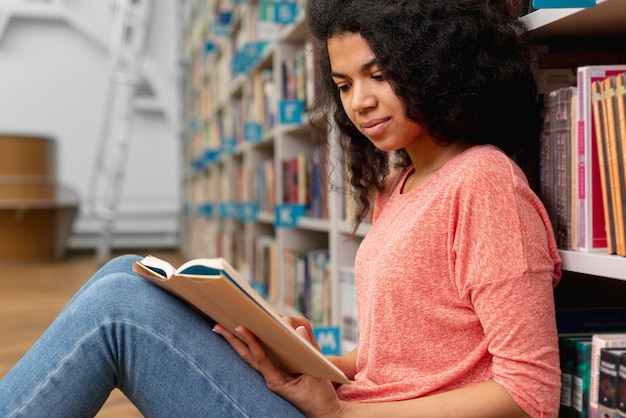 Chica de ángulo bajo en la biblioteca en el piso leyendo