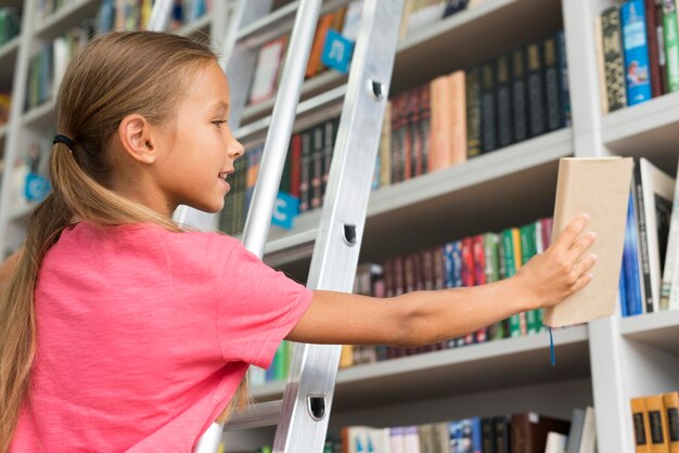 Chica de ángulo bajo colocando un libro en el estante