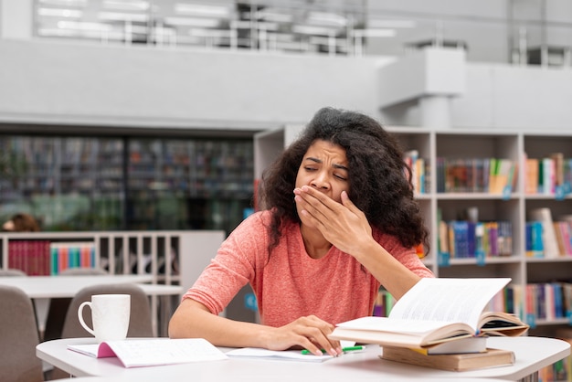 Chica de ángulo bajo con sueño en la biblioteca