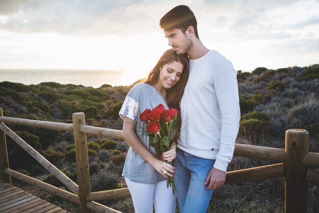 Chica apoyada en su novio mientras sujeta un ramo de rosas