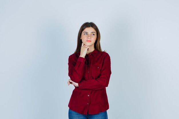 chica apoyando la barbilla en la mano, mirando a otro lado con una camisa color burdeos y mirando pensativa.