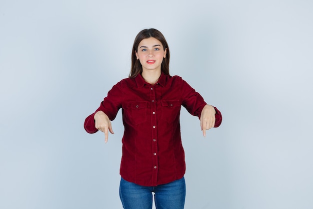 Foto gratuita chica apuntando hacia abajo en blusa burdeos y mirando alegre