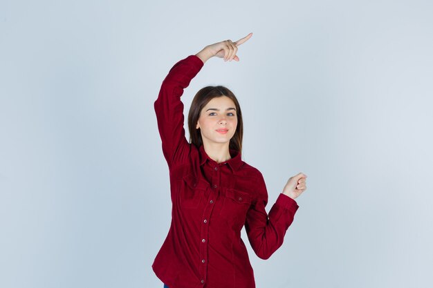 chica apuntando a la esquina superior derecha con camisa casual y mirando confiada.