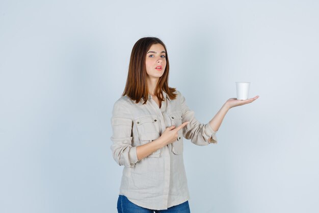 chica apuntando a una taza de café de plástico en camisa y mirando vacilante.