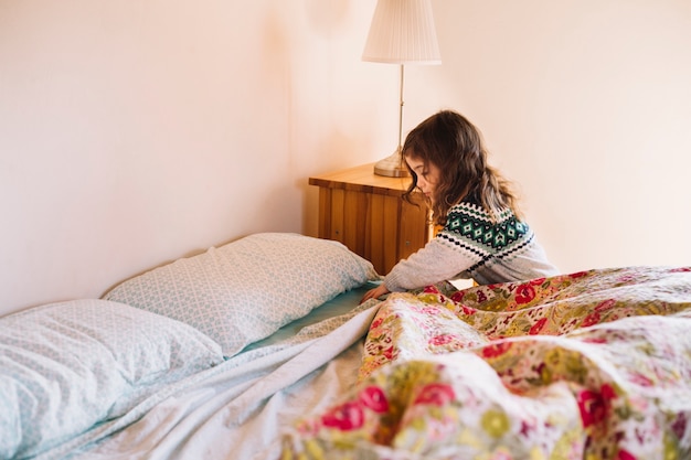 Chica arreglando sábana en el dormitorio