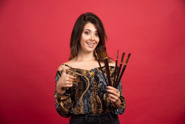 Chica artista demostrando su conjunto de nuevos pinceles de marca y se ve satisfecha.