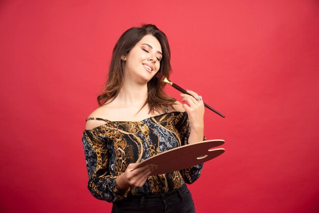 Chica artista posando con su tablero de paleta de madera y pincel.