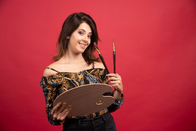 Chica artista posando con su tablero de paleta de madera y pincel.