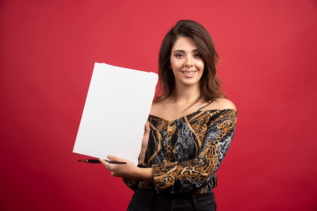 Chica artista sosteniendo su obra de arte sobre lienzo y mostrándola al público.