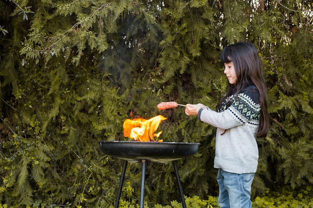 Foto gratuita chica asar salchichas sobre la llama en barbacoa al aire libre