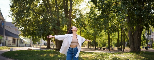 Foto gratuita chica asiática despreocupada bailando sintiendo felicidad y alegría disfrutando del sol en el día de verano caminando en el parque