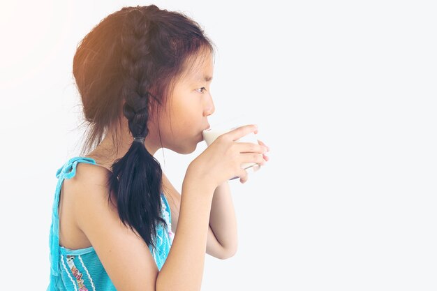 Chica asiática está bebiendo un vaso de leche sobre fondo blanco