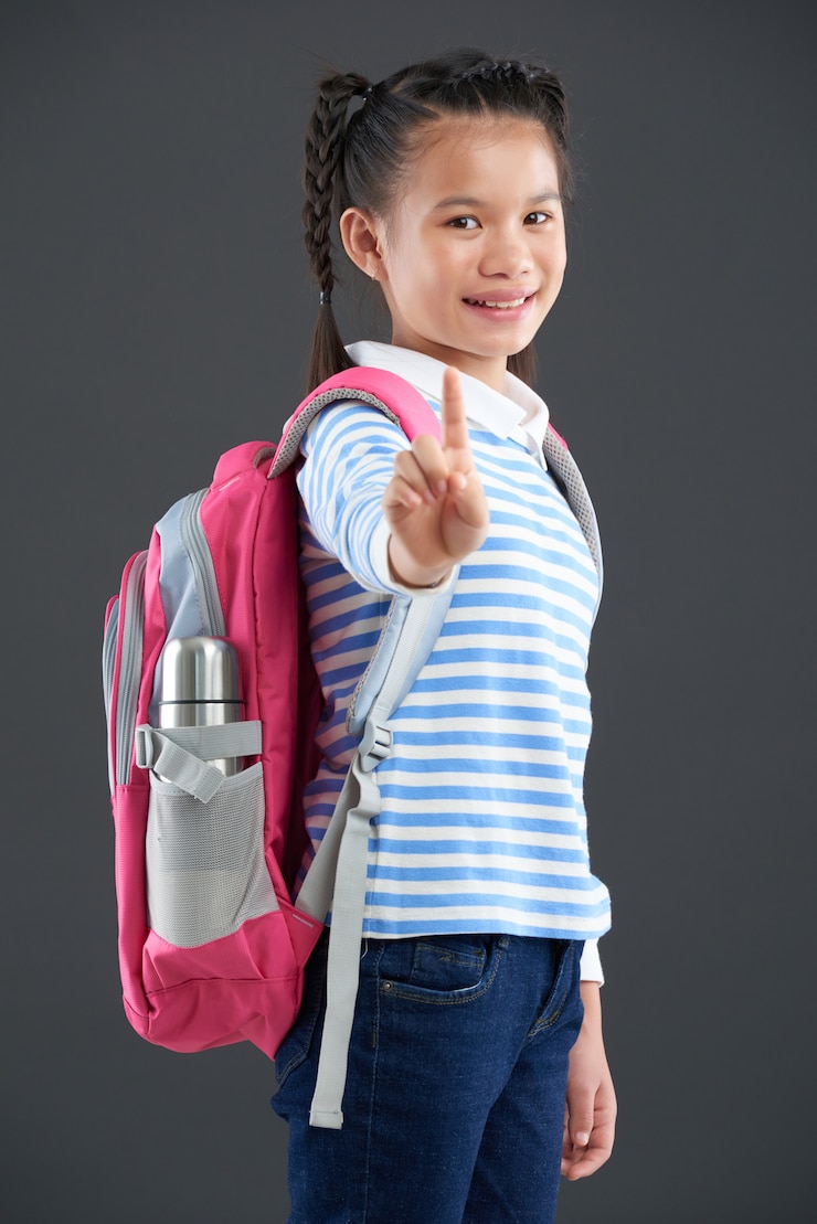 Foto gratuito chica asiática con mochila de pie y mostrando un dedo índice a la cámara