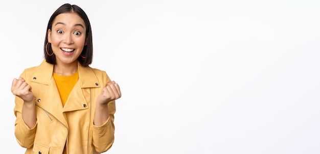 Chica asiática sorprendida y feliz mirando con cara feliz de regocijo ganando celebrando la victoria y triunfando de pie sobre fondo blanco