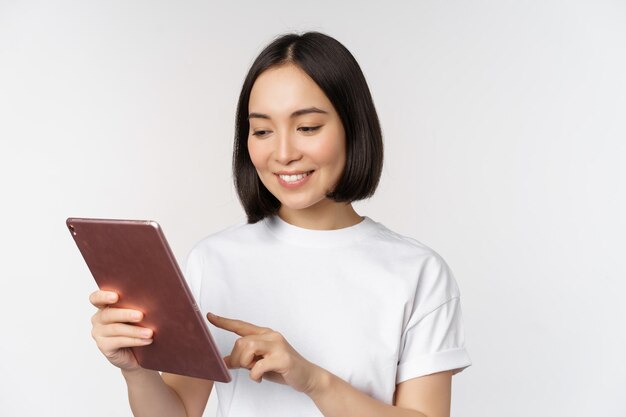 Chica asiática usando tableta digital trabajando con compras de gadgets en línea de pie sobre fondo blanco.