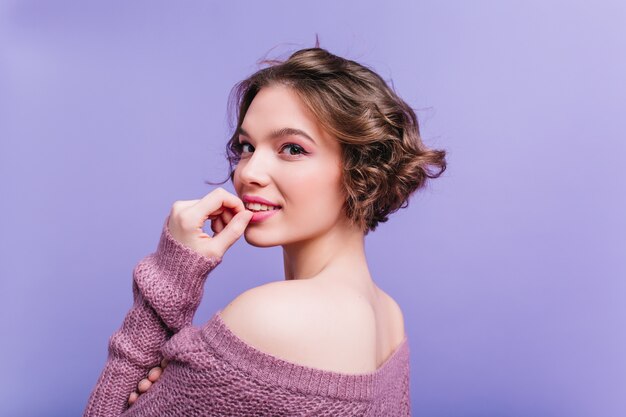 Chica asombrosa en bufanda de punto larga gritando con los ojos cerrados. Magnífica dama europea en ropa de invierno con estilo posando en la pared púrpura