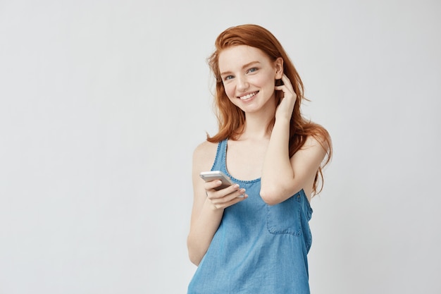 Chica astuta sincera alegre con pecas sonriendo sosteniendo el teléfono.