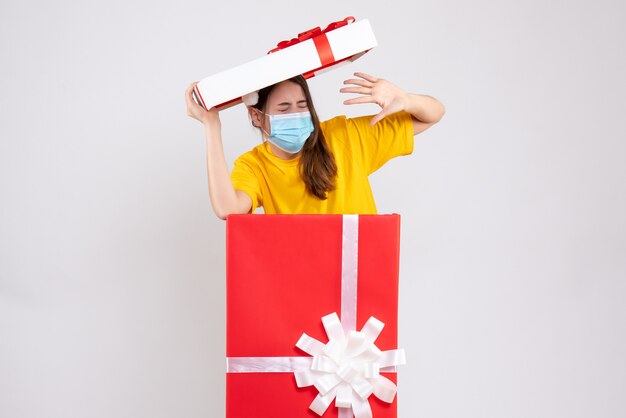 Foto gratuita chica asustada con gorro de papá noel de pie detrás de un gran regalo de navidad en blanco