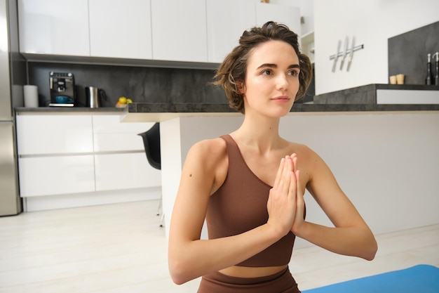 Chica atleta deportista sonriente haciendo yoga en casa en ropa deportiva sentada en una alfombra de goma de yoga en lotu