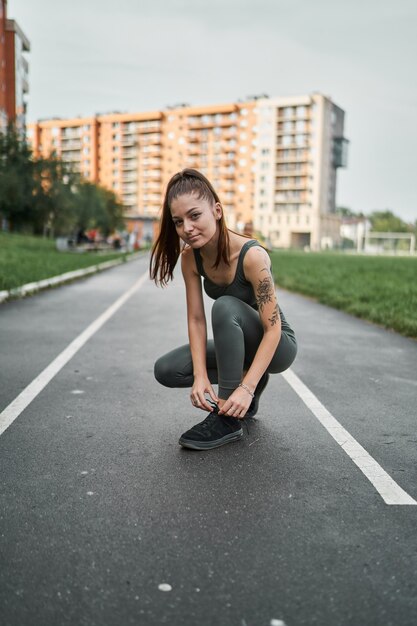 Chica atlética ata los cordones de sus zapatos en el estadio.