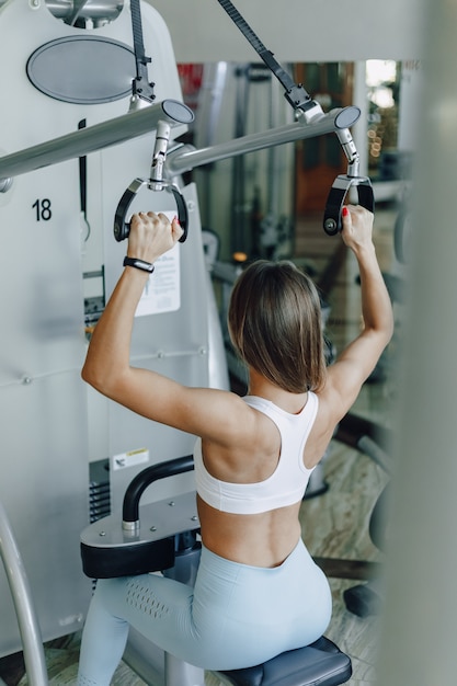 Chica atlética atractiva entrena hombros en simulador. Vista de los músculos de la espalda. estilo de vida saludable.