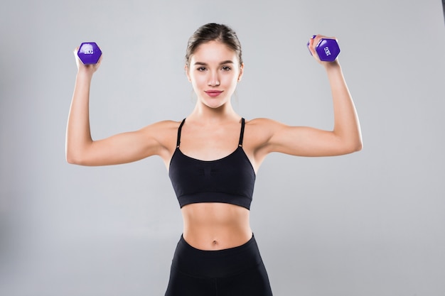 Chica atlética fitness con pesas en una pared blanca