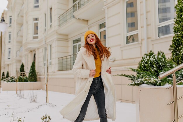 Chica atractiva en bata blanca bailando en la calle. Modelo femenino europeo atractivo que presenta con sonrisa en invierno.