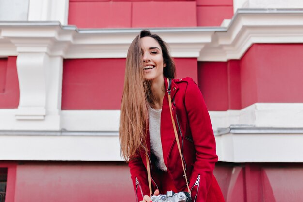 Chica atractiva con cabello castaño posando en la ciudad con cámara