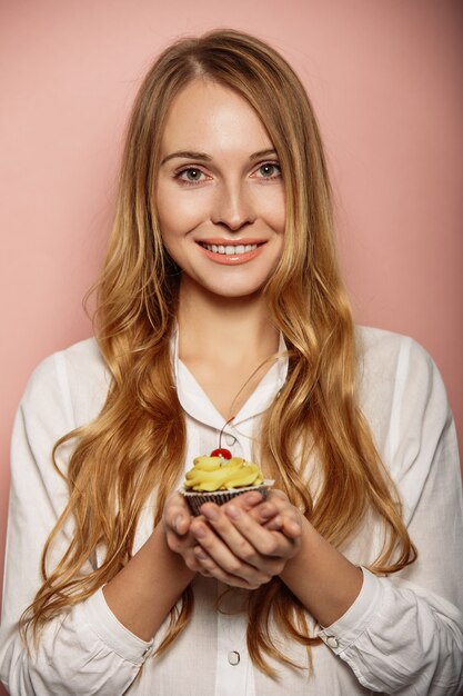 Chica atractiva con una camisa blanca está sosteniendo cupcakes