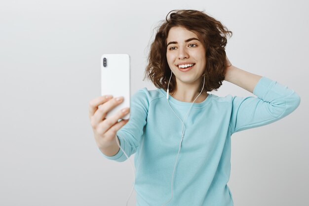 Chica atractiva feliz tomando selfie en smartphone, posando con auriculares