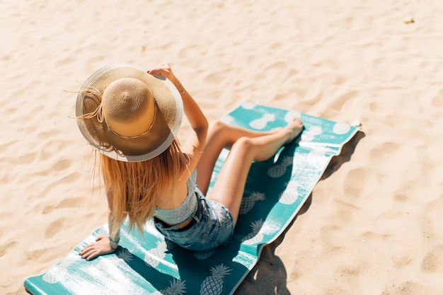 Chica atractiva con gafas de sol y sombrero se encuentra en arena cálida