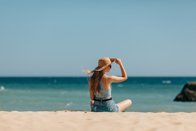 Chica atractiva con gafas de sol y sombrero se encuentra en arena cálida