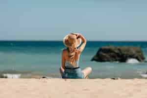 Foto gratuita chica atractiva con gafas de sol y sombrero se encuentra en arena cálida