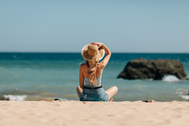 Chica atractiva con gafas de sol y sombrero se encuentra en arena cálida