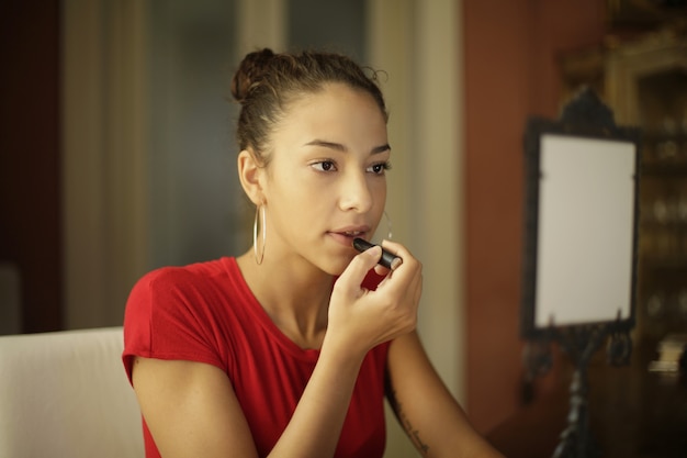 Foto gratuita chica atractiva joven arreglando su maquillaje frente al espejo en la habitación