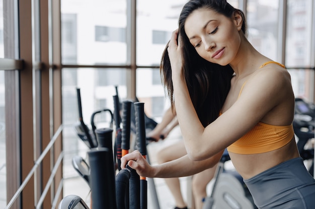 Chica atractiva joven en el gimnasio en bicicleta de ejercicio, fitness y yoga