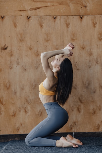 Chica atractiva joven haciendo ejercicios de fitness con yoga en el piso sobre un fondo de madera