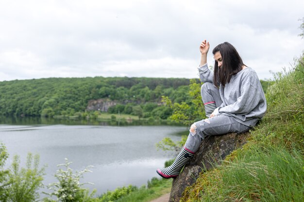 Una chica atractiva en un paseo subió un acantilado en una zona montañosa y disfruta del paisaje.