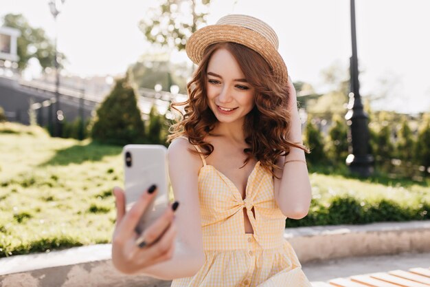 Chica atractiva con peinado rizado haciendo selfie en parque. Bastante joven jengibre tomando una foto de sí misma mientras descansa al aire libre.