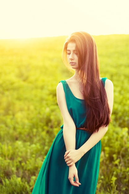 Chica atractiva posando con un vestido verde al atardecer