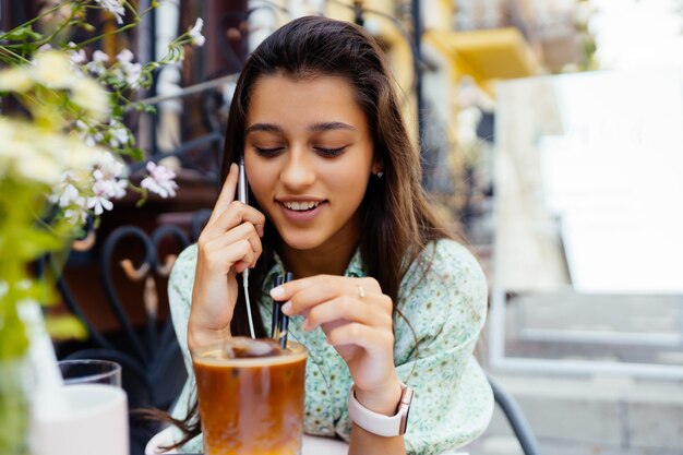 Chica atractiva sentada al aire libre en la calle café, hablando de smartphone