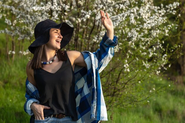 Chica atractiva con un sombrero entre los árboles en flor en la primavera, en un estilo casual