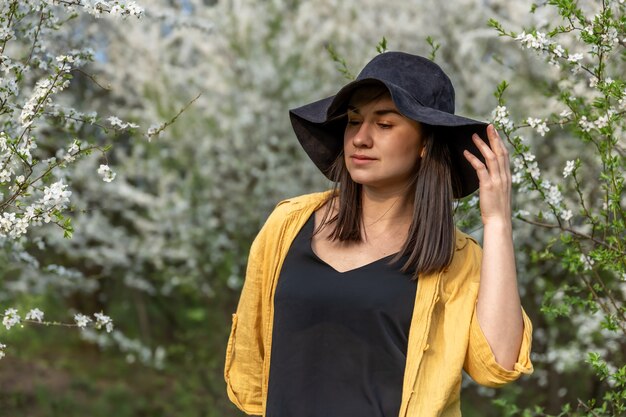 Chica atractiva con un sombrero entre los árboles en flor en la primavera, en un estilo casual