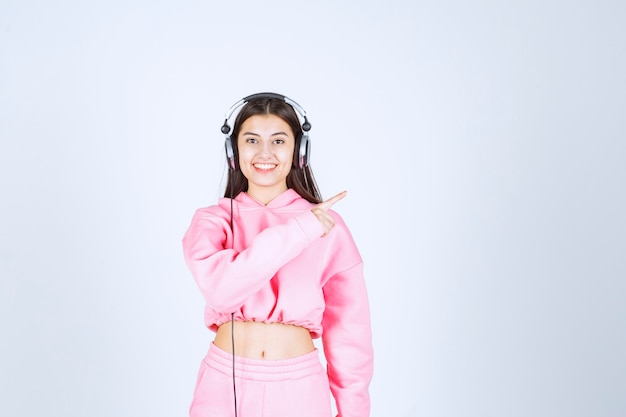 Chica con auriculares y apuntando hacia el lado derecho. Foto de alta calidad