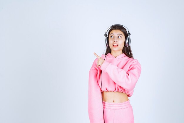 Chica con auriculares y apuntando hacia el lado izquierdo. Foto de alta calidad